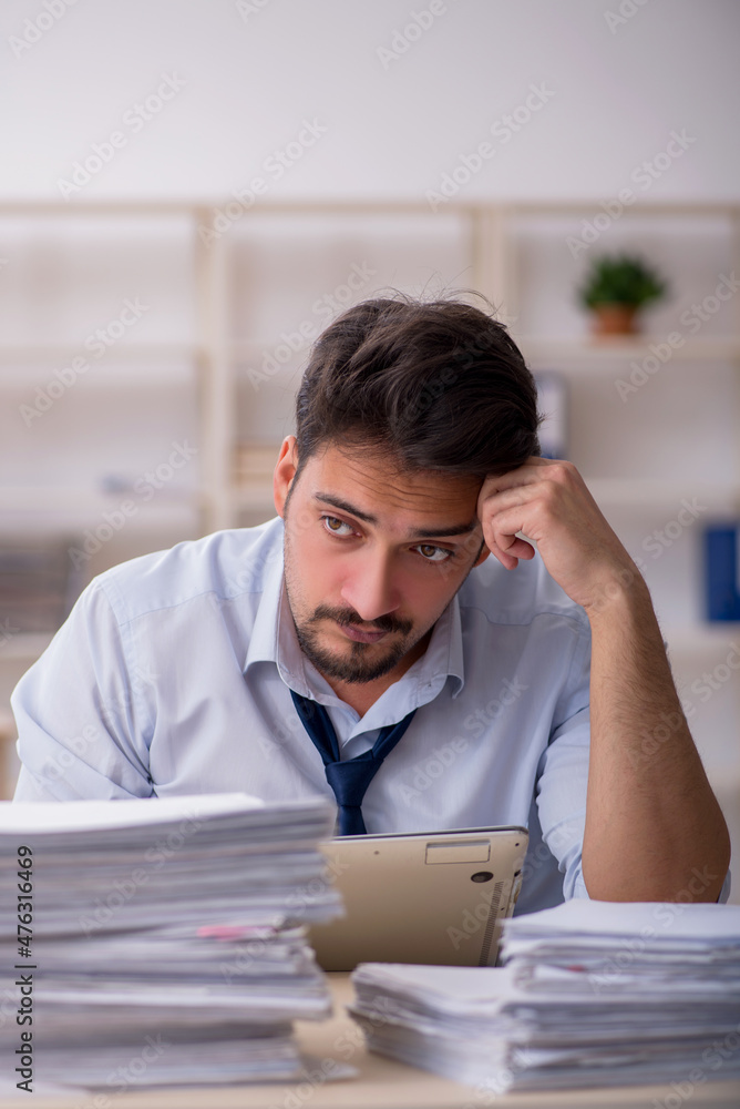 Young male employee unhappy with excessive work in the office Young male employee unhappy with excessive work in the office