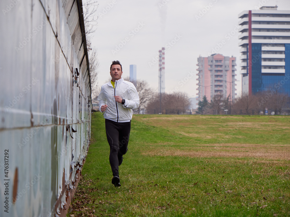 Adult Man running in the parc in winter with city background Adult Man running in the parc in winter with city background