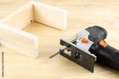Electric jigsaw. Woodworking power tools. Jigsaw in hand. Wooden planks. To the Workshop. On a wooden table. Desktop. Workplace.