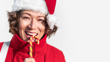 Curly winking woman in Santa Claus hat bites striped candy cane. Pretty female with Christmas licorice whip. Banner with copy space.