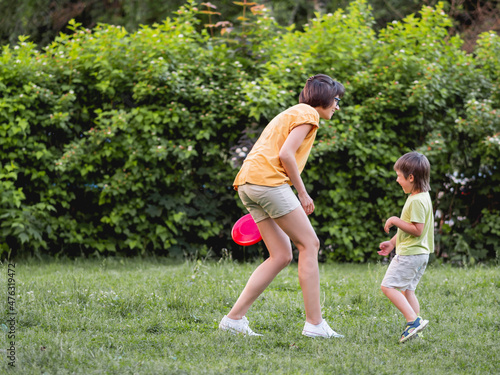 Mother and son play frisbee on grass lawn. Summer vibes. Outdoor leisure activity. Family life. Sports game at backyard.