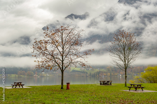 Moody autumn landscape with bare trees and benches on mountain lake shore.