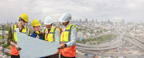 Industry manager with engineers meeting developer holding blueprint on the roof with blurred urban background