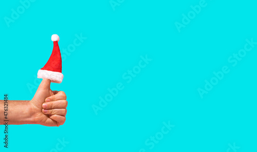 Santa Claus hat is put on the finger on blue background. Hand is holding thumbs up. Creative Christmas and New Year idea. Minimal announcement or like idea. Social network concept. Copy space.