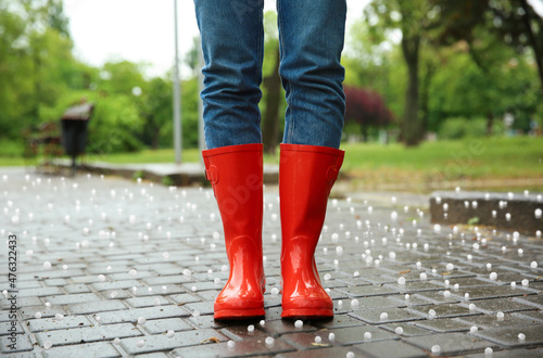Woman wearing red rubber boots outdoors after thunderstorm with hail, closeup