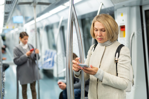 Adult woman browsing and typing messages on tablet in subway car leaning on handrail. High quality photo
