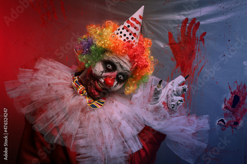 Fototapeta Naklejka Na Ścianę i Meble -  Terrifying clown near bloodstained plastic film. Halloween party costume