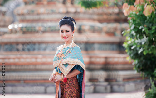 Portrait of a beautiful woman wearing a traditional Thai dress smiling gracefully standing in a temple of Thailand