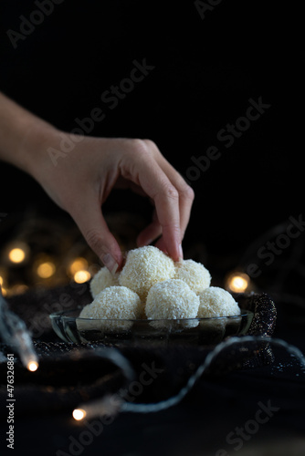 Coconut balls, typical czech christmas candy, still life with homemade confectionery with lights in the background, raw, easy, vegan, woman hand