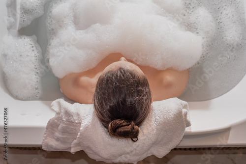 Woman relaxing in hot bath tub with soap foam