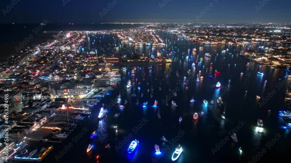 Christmas celebration in Newport beach with colorful boat parade. Bright illuminated boats sailing around Balboa island in the bay at night. Cinematic aerial hyper lapse of winter season holidays fest