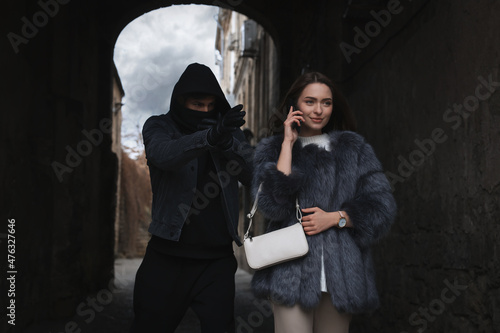 Criminal attacking young woman while she talking on phone in alley. Self defense concept photo