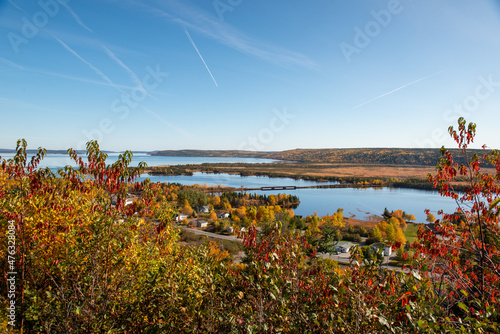 A marsh and barren land with a large river in the center in autumn. There are trees, shrubs, and large boulders and rocks scattered across the ground. The sky is blue with layers of thick clouds.