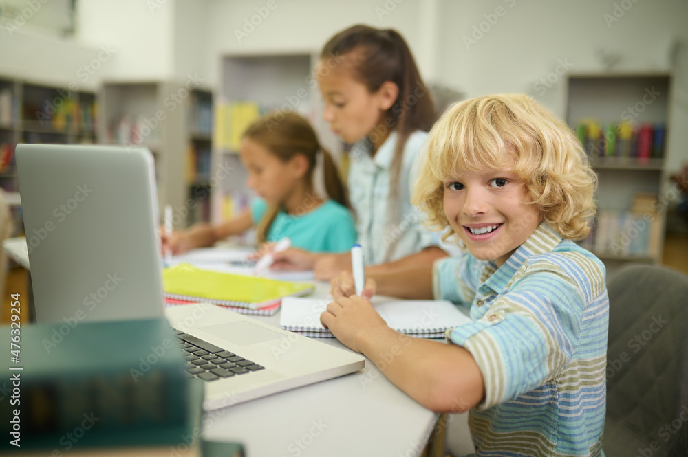 Boy sitting at table looking at camera and girls Boy sitting at table looking at camera and girls