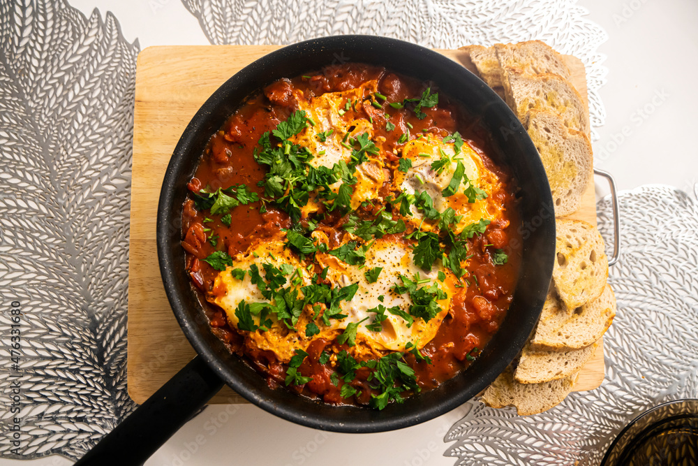 Shakshouka with tomatoes, peppers eggs, on a hot pan with crout croutons sprinkled with chives Shakshouka with tomatoes, peppers eggs, on a hot pan with crout croutons sprinkled with chives