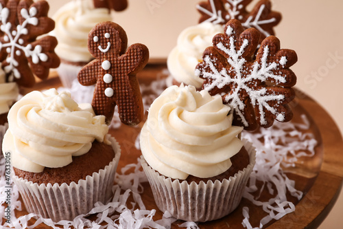 Wooden stand of tasty Christmas cupcakes with gingerbread cookies on beige background, closeup