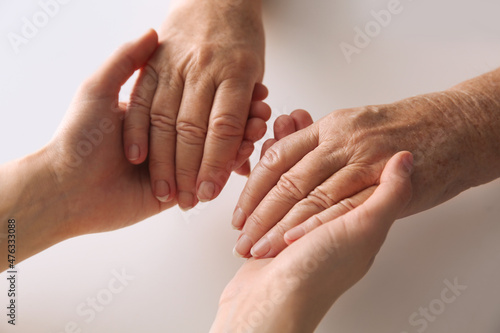 Fototapeta Naklejka Na Ścianę i Meble -  Young and elderly women holding hands together at white table, closeup