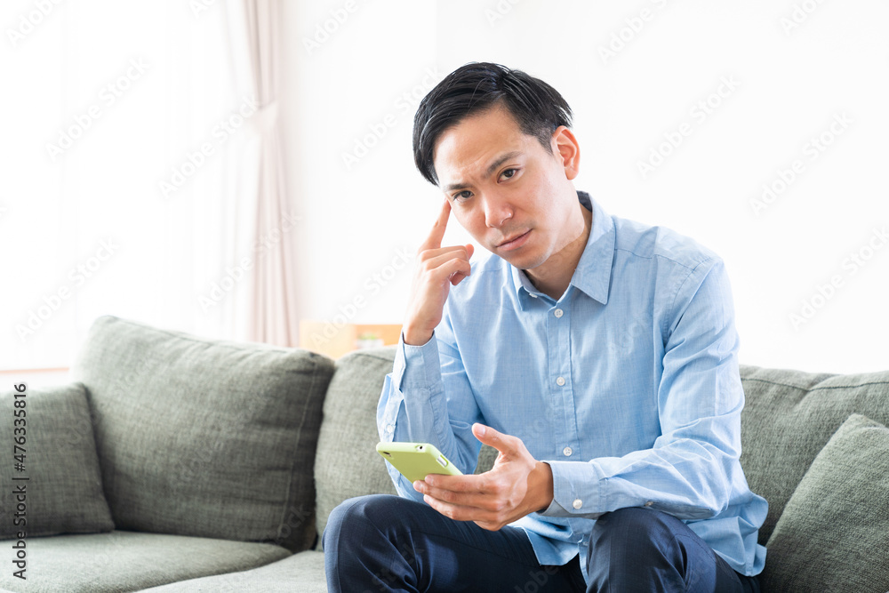 部屋でスマホを見る男性　考える