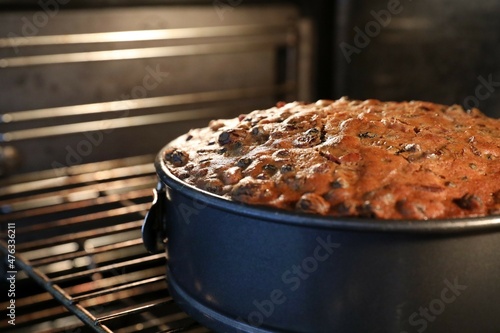 A close up of a delicious golden brown traditional fruit or festive Christmas cake still in the oven. Round baking tin and oven tray with perfectly cooked cake rising.