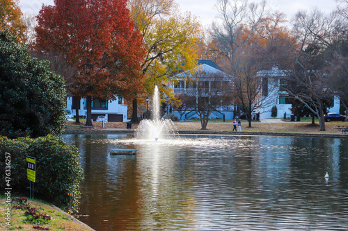 Fototapeta Naklejka Na Ścianę i Meble -  a water fountain in the middle of a still lake surrounded by red and yellow autumn colored trees in the park with fallen autumn leaves on the ground at Freedom Park in Charlotte North Carolina USA	
