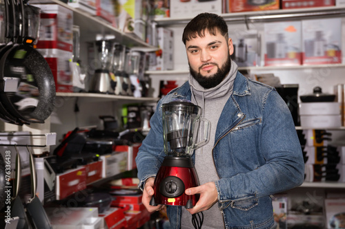 Adult glad positive smiling male is standing with new mixer for his home in the store