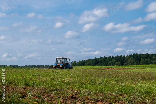 Tractor working in the field, plowing the land, preparing for sowing. View of the field and tractor in the distance against a blue sky with clouds