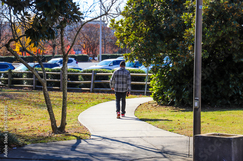 an African American man walking on a smooth winding footpath in the par surrounded by lush green and autumn colored trees at Marshall Park in Charlotte USA