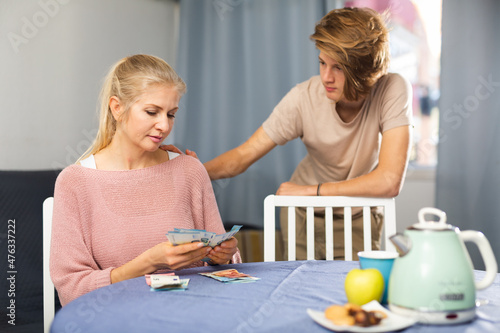 Obraz na plátne Adult woman sitting at home table counting family budget while her teenage son s