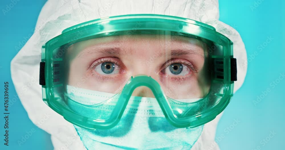 A doctor in medical glasses and a protective hood is looking at us. close-up A doctor in medical glasses and a protective hood is looking at us. close-up
