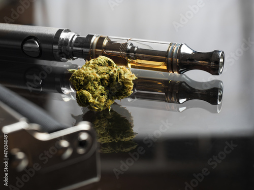 Close up shot of real cannabis or weed with cannabis oil in cartridge of vape  pen in the background, roller blurred in foreground and text space on the right under the dark theme