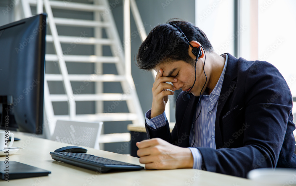 Asian stressed depressed upset telemarketer receptionist operator service support male employee staff in formal suit wears headset holding hand on head having headache when working overload overtime Asian stressed depressed upset telemarketer receptionist operator service support male employee staff in formal suit wears headset holding hand on head having headache when working overload overtime