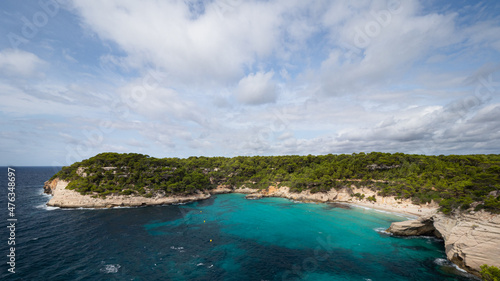 Cala Mitjana y Mitjaneta en Menorca, Islas Baleares, España, con su agua de color turquesa y su arena dorada en un día soleado. Gente bañandose y tomando el sol.