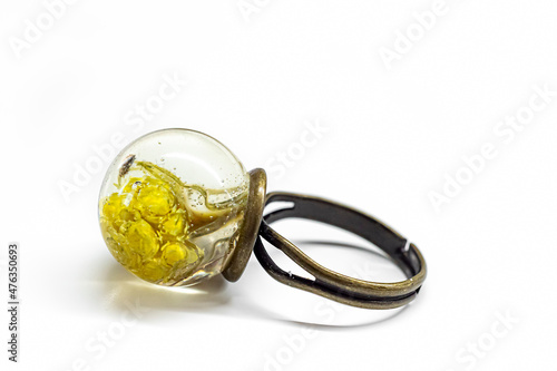 Macro photography of handmade jewelry. Yellow dwarf everlast flower inside epoxy resin ring with brass base. Selective focus on the details, blurred background.