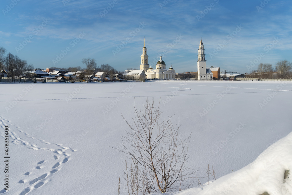 The historical center of the city of Nevyansk (Russia) with its famous leaning tower and church on a sunny winter day. View from the high bank of the city pond. Gentle winter landscape with clean snow