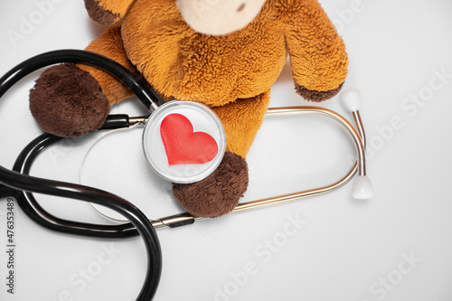 Small red heart and a stethoscope or phonendoscope with a plush toy on a white background, top view: pediatric cardiology, blood donor for children. Background of Health and Medicine