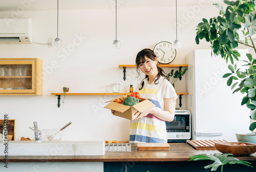 キッチンでダンボールに入った野菜を持つ女性 