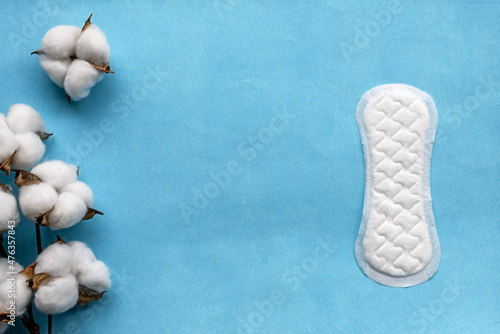 Cotton flower on blue paper background and sanitary pads for women, top view. The concept of hygiene and women's health