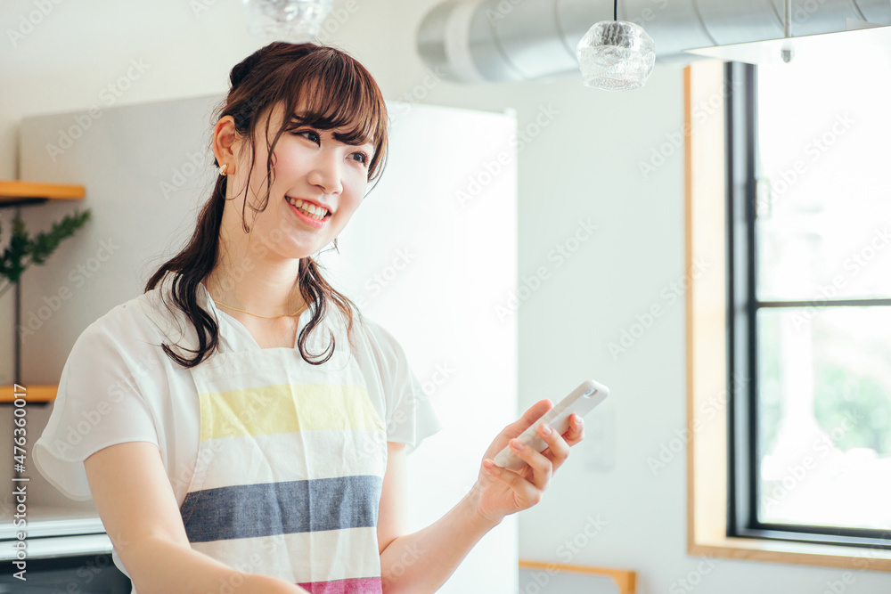 キッチンでスマホを持つ女性(スマホ・笑顔)
キッチンでスマホを持つ女性(スマホ・笑顔)