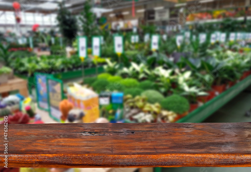 Wooden board on a background of blurred shop. Shop with plants and seedlings. Sharpness on the board. Place for product advertising. Free space for design and goods. Layout for products.