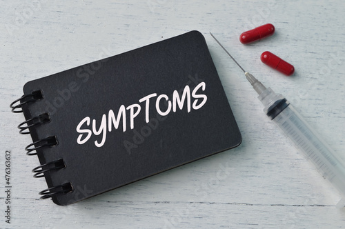 Syringe injection, pill capsules and notebook with text SYMPTOMS