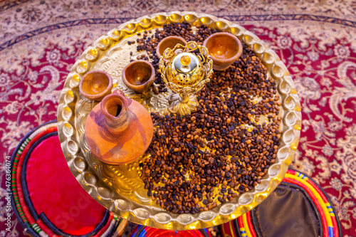 Caffe mocha coffee grains and arabic incenses on a golden tray with clay jugs and bowls, traditional Yemeni coffee table with colorful arabic majlis cushions. photo