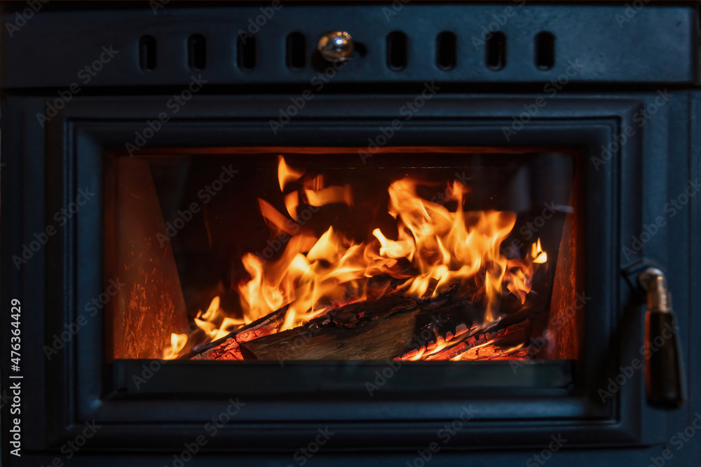 Fototapeta premium Burning fire in a wood stove fireplace radiates heat, warm home interior,