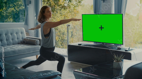 Foto Attractive fit girl doing yoga in living room with Green Screen TV