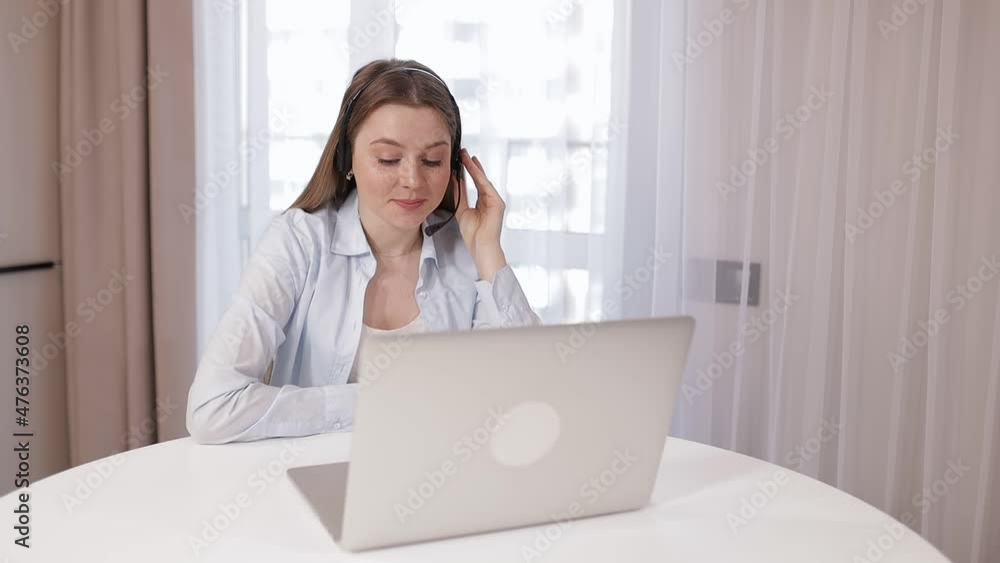 Friendly businesswoman in wireless headphones with microphone starting an online meeting with a webcam video call with colleagues