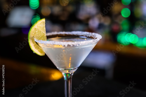 In a funnel-shaped glass with a long stem, the alcoholic cocktail is opaque, opaque, with a slice of lime on the sugared edge of the glass. Filming of the bar menu against the background