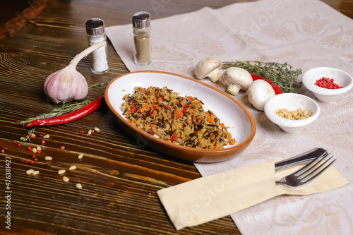 On a dark countertop Pilaf .In an oval dish, pilaf with black rice is served, on a linseed sallet, cutlery, a pair of salt and pepper, spices