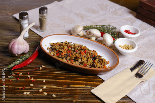 On a dark countertop Pilaf .In an oval dish, pilaf with black rice is served, on a linseed sallet, cutlery, a pair of salt and pepper, spices