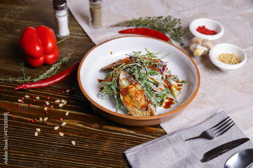 On a dark countertop, a light linen napkin, on a cutting board  Salad with mussels, rucola, red caviar, shrimps in a round dish, cutlery, pepper-salt steam, whole red pepper, hot pepper pod
