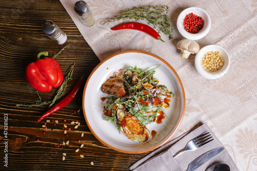 On a dark countertop, a light linen napkin, on a cutting board  Salad with mussels, rucola, red caviar, shrimps in a round dish, cutlery, pepper-salt steam, whole red pepper, hot pepper pod