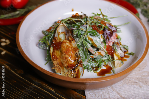 On a dark countertop, a light linen napkin, on a cutting board  Salad with mussels, rucola, red caviar, shrimps in a round dish, cutlery, pepper-salt steam, whole red pepper, hot pepper pod